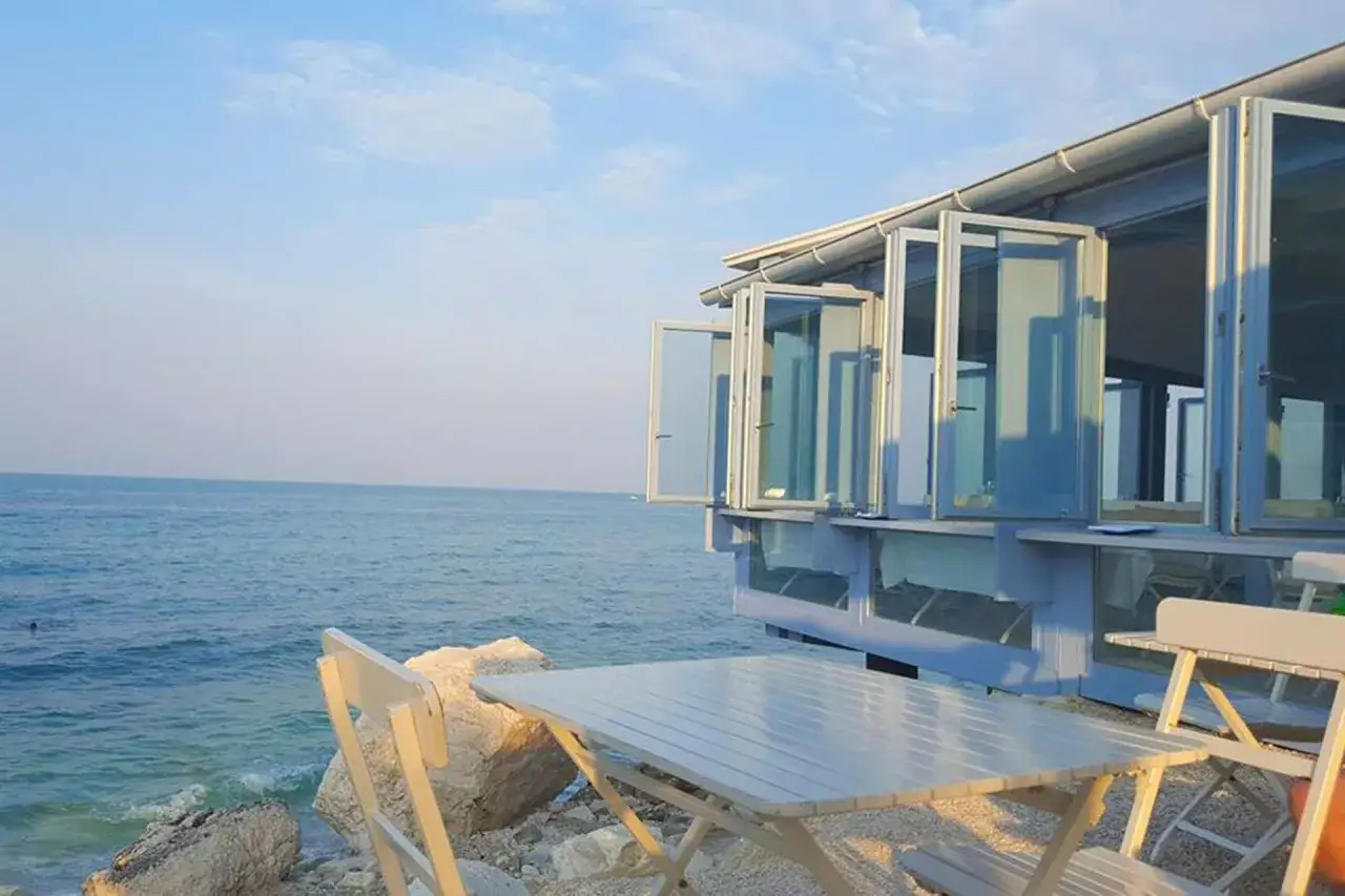 Tavoli e sedie all'aperto di ristoranti Rimini sul mare, con il blu dell'Adriatico e il cielo limpido.
