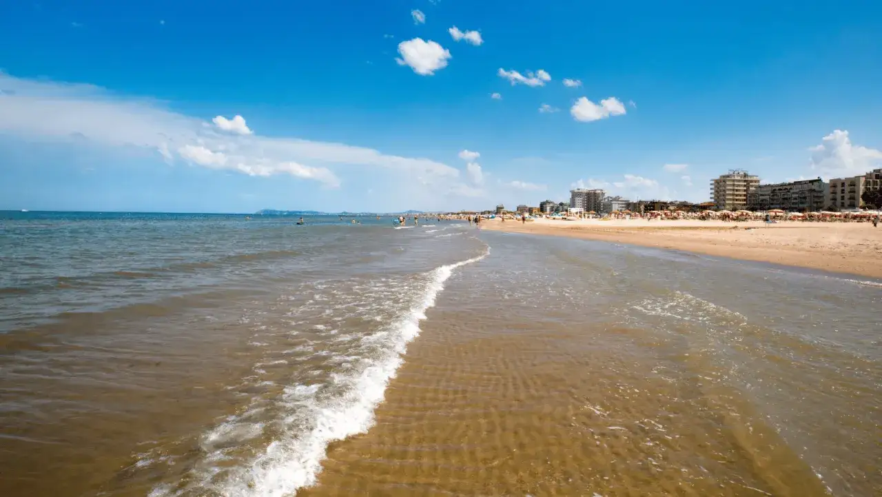 Onda leggera sul mare Adriatico, con la spiaggia affollata e gli hotel sullo sfondo. Un classico giorno d'estate in Emilia-Romagna.
