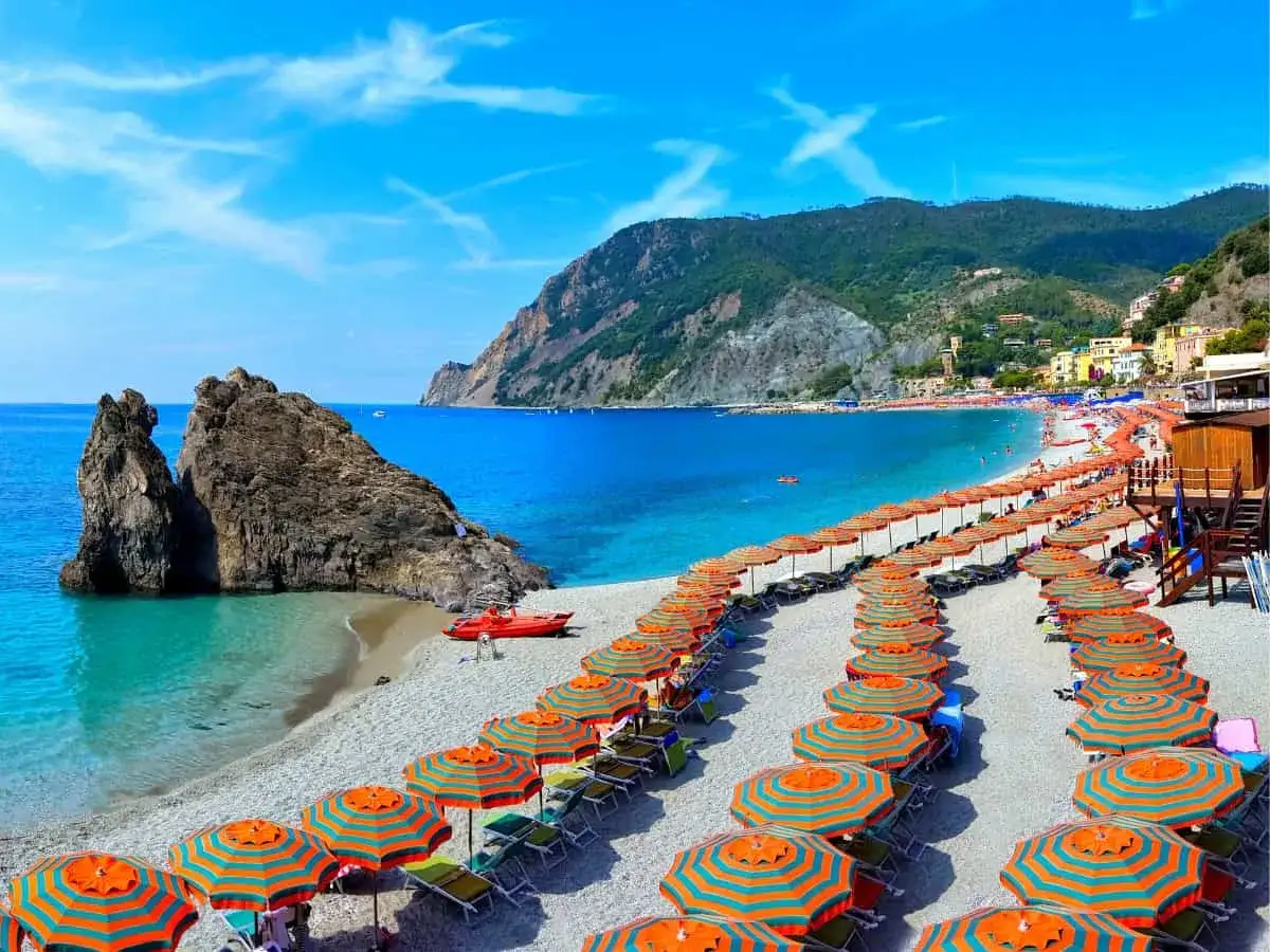 Una splendida spiaggia libera attrezzata con file di ombrelloni colorati, lettini, un mare azzurro e una scogliera imponente.