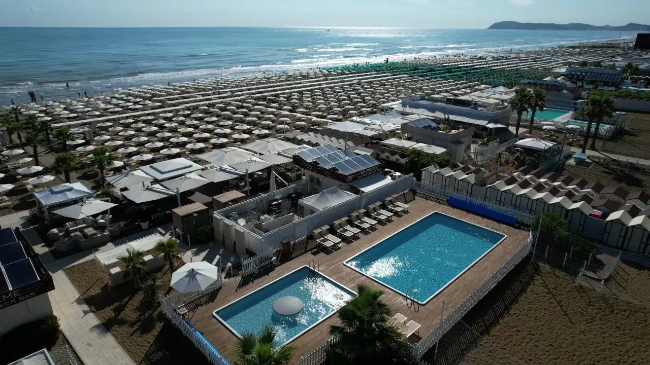 Vista aerea della spiaggia Le Palme a Riccione con ombrelloni, piscine e cabine.