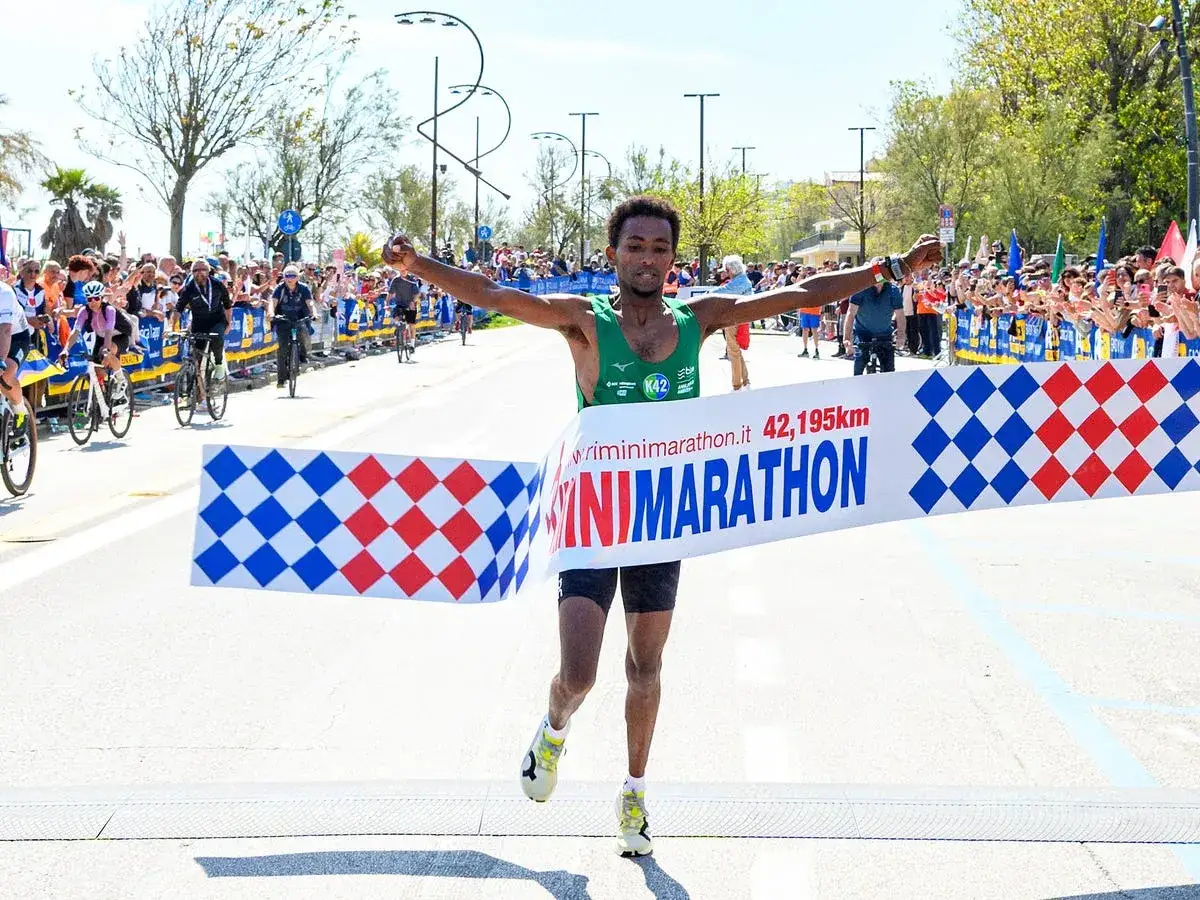 Vincitore della Rimini Half Marathon taglia il traguardo con le braccia alzate, acclamato dalla folla.