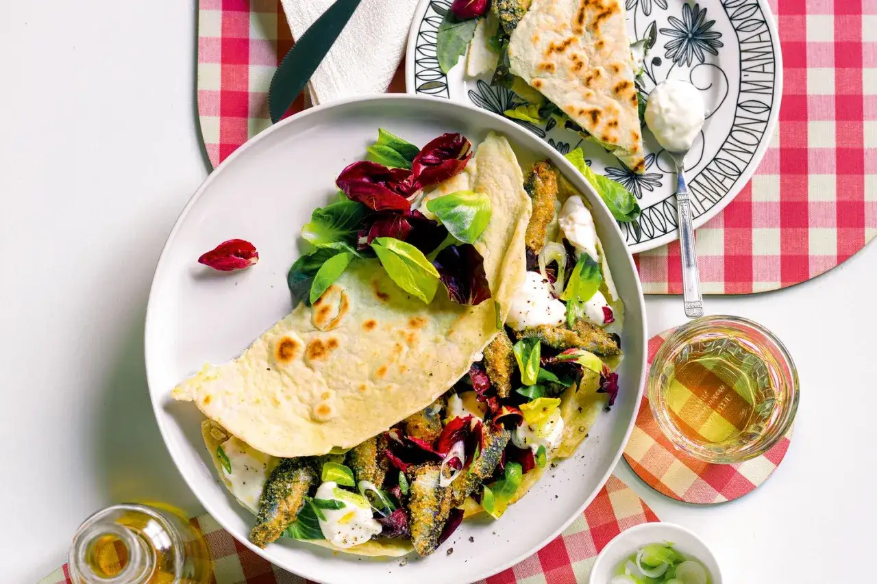 Piadina ripiena di sardoncini alla romagnola, insalata fresca e formaggio cremoso, servita con un bicchiere di vino bianco.
