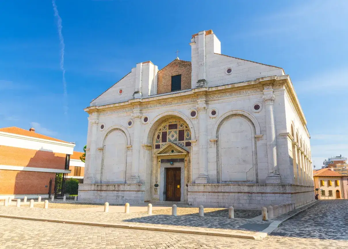 La facciata bianca e imponente della chiesa San Francesco a Rimini, sotto un cielo azzurro.