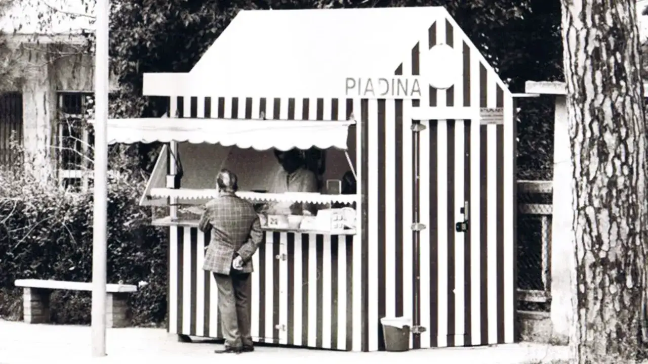 Un uomo ordina una piadina in un chiosco a strisce, un'immagine che evoca l'origine di questo street food.