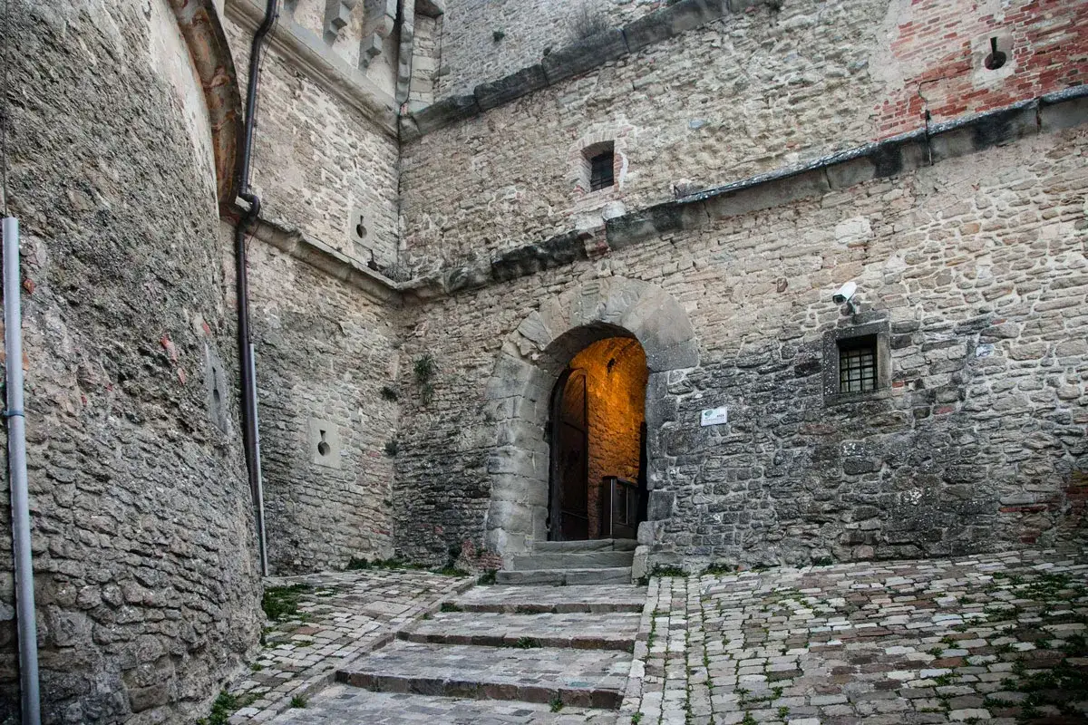 Ingresso alla fortezza di San Leo, con un arco in pietra illuminato e una scalinata che conduce all'interno.