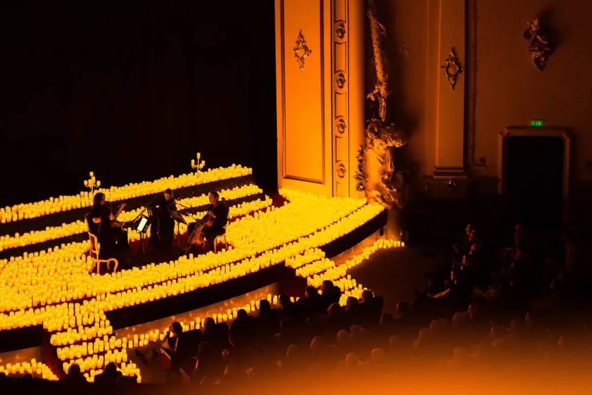 Un trio d'archi suona su un palco illuminato da migliaia di candele, creando un'atmosfera magica per un concerto a Rimini.