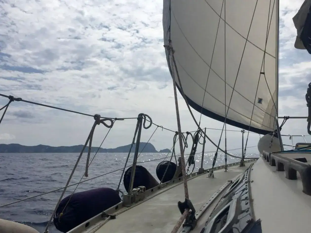 Vela bianca gonfiata dal vento, mare calmo e isole all'orizzonte. Un'avventura in barca, come in un club nautico.