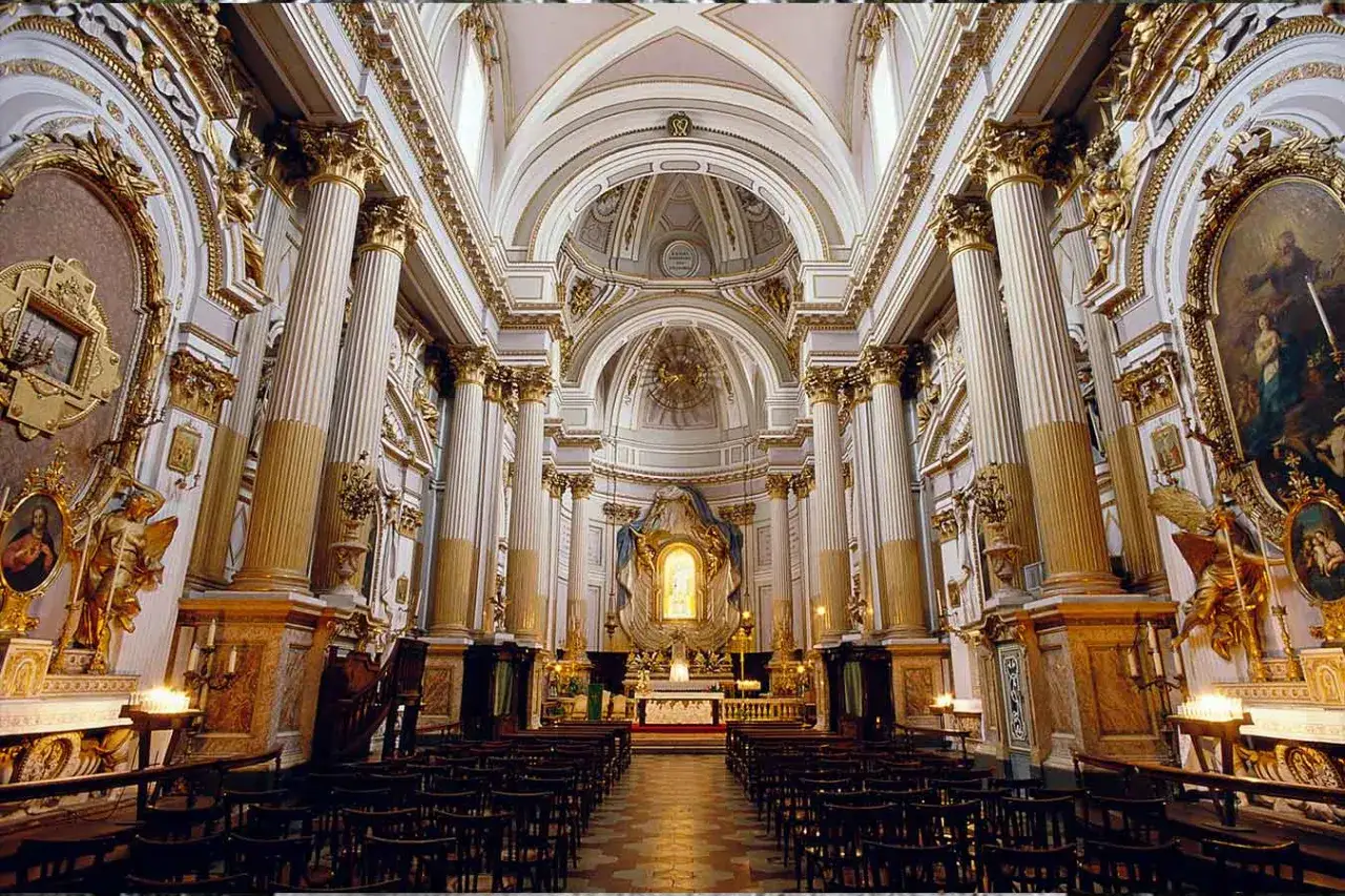 Interno sfarzoso di una chiesa a Rimini, con colonne dorate, affreschi e un altare illuminato.