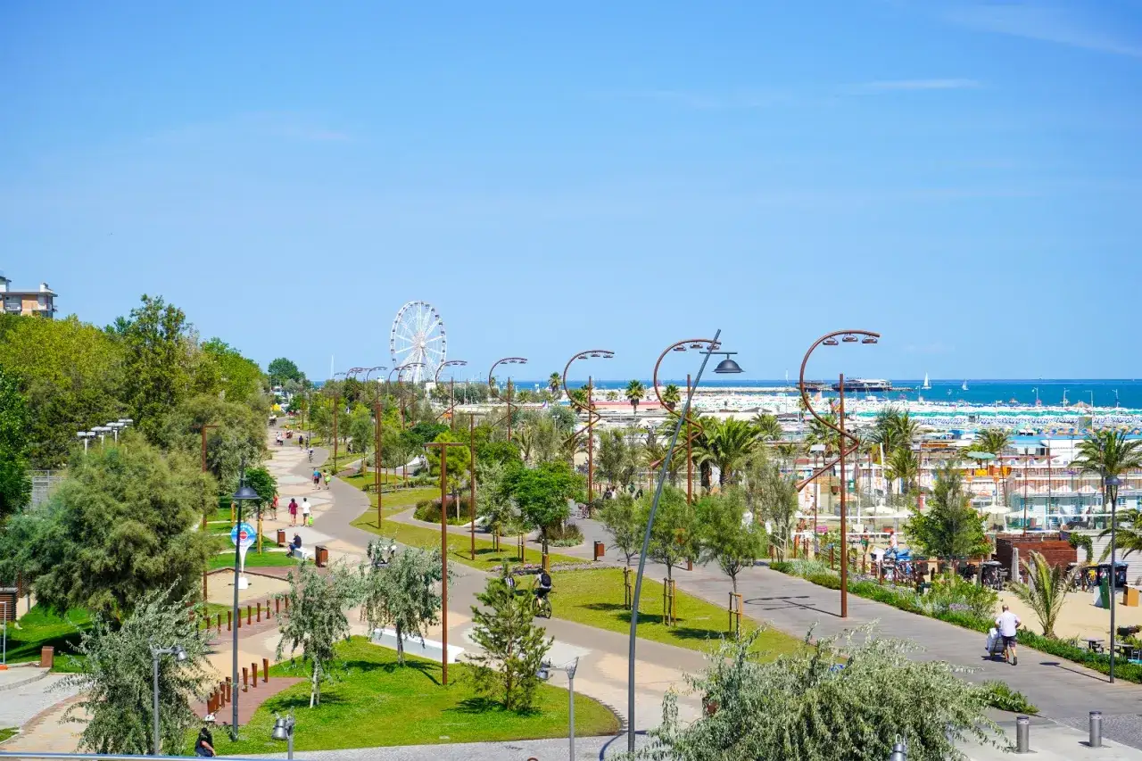 Passeggiata sul lungomare di Piazzale Kennedy a Rimini, con gente che cammina e pedala, la ruota panoramica e il mare sullo sfondo.