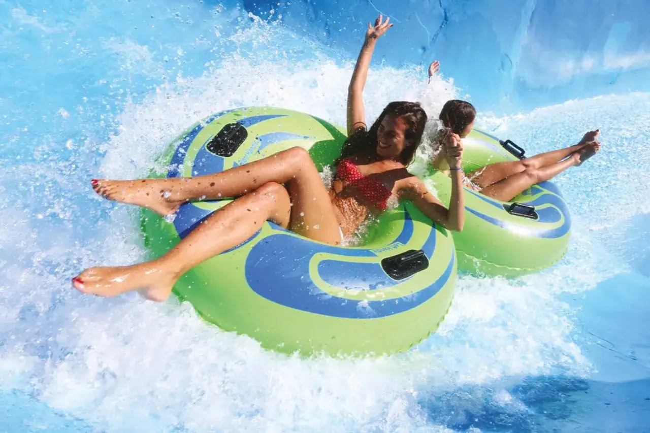 Due ragazze ridono su ciambelle gonfiabili in un parco acquatico, scendendo veloci come su delle montagne russe.