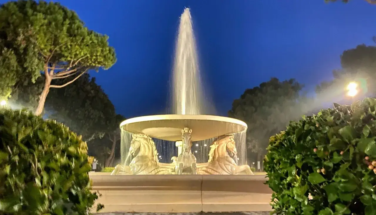 Fontana con cavalli marini nel Parco Federico Fellini a Rimini, illuminata di notte sotto un cielo blu intenso.