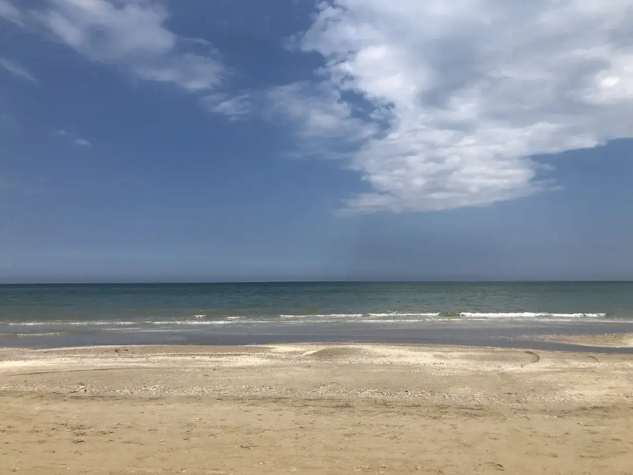 Spiaggia di sabbia dorata, mare calmo e cielo azzurro con nuvole bianche. Un perfetto week end a Rimini, con la brezza marina che accarezza la riva.