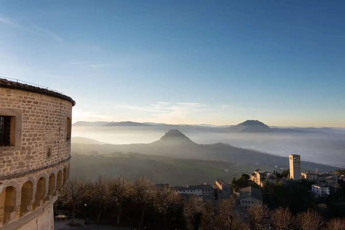 Vista panoramica di borghi vicino Riccione, con un castello in primo piano e colline nebbiose all'orizzonte.