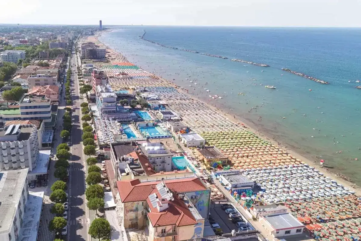 Vista aerea del lungomare Valverde di Cesenatico, con la spiaggia affollata di ombrelloni e bagnanti, piscine e palazzi.
