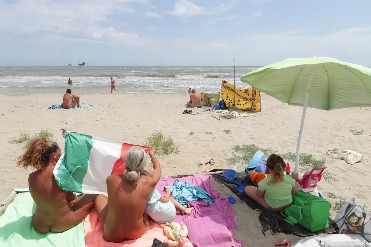 Persone rilassate sulla spiaggia della Bassona, una sventola la bandiera italiana.