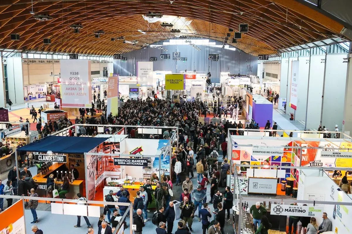 Folla in un padiglione fieristico, un'attrazione beer&food con stand e degustazioni.