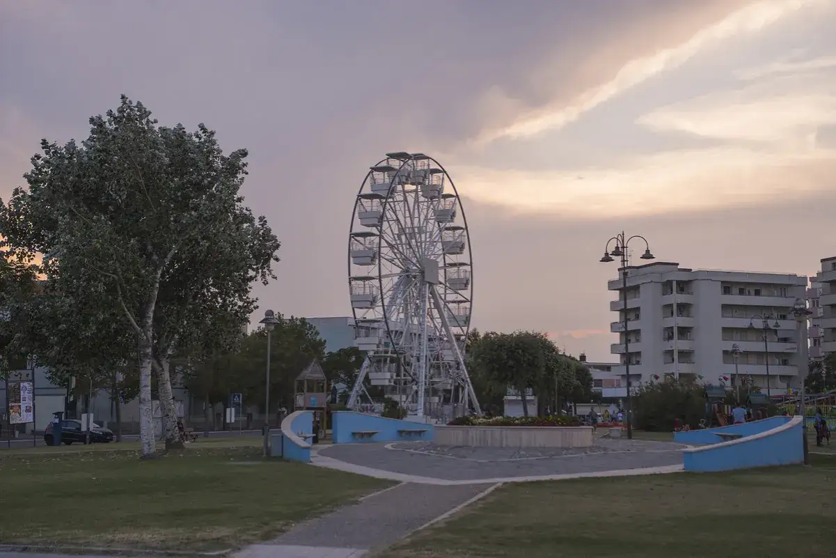 Ruota panoramica al tramonto nel centro di Gatteo Mare, con edifici residenziali sullo sfondo e un parco giochi.