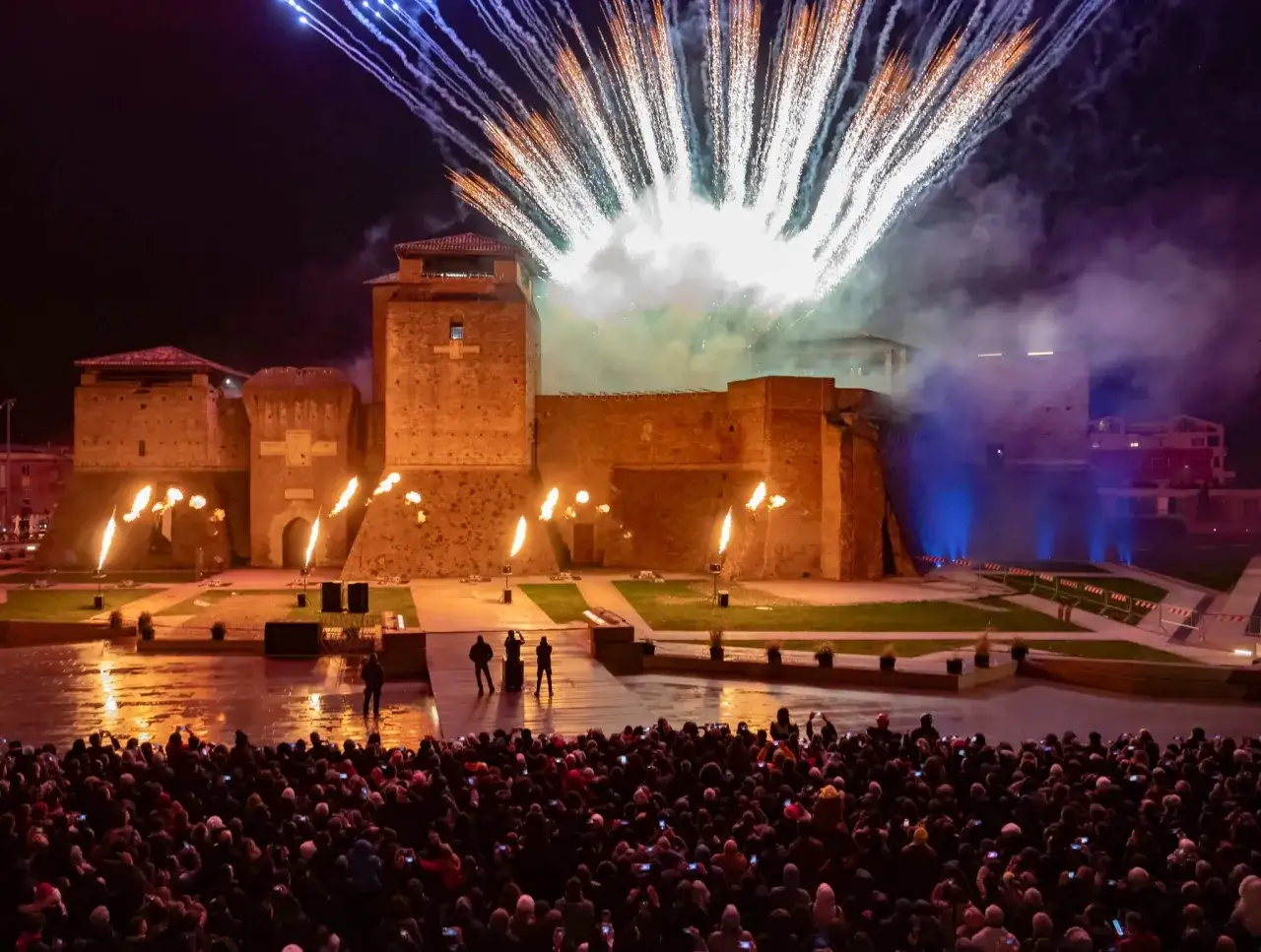 Spettacolare capodanno in riviera romagnola con fuochi d'artificio che illuminano un castello medievale, mentre una folla festante ammira lo show.