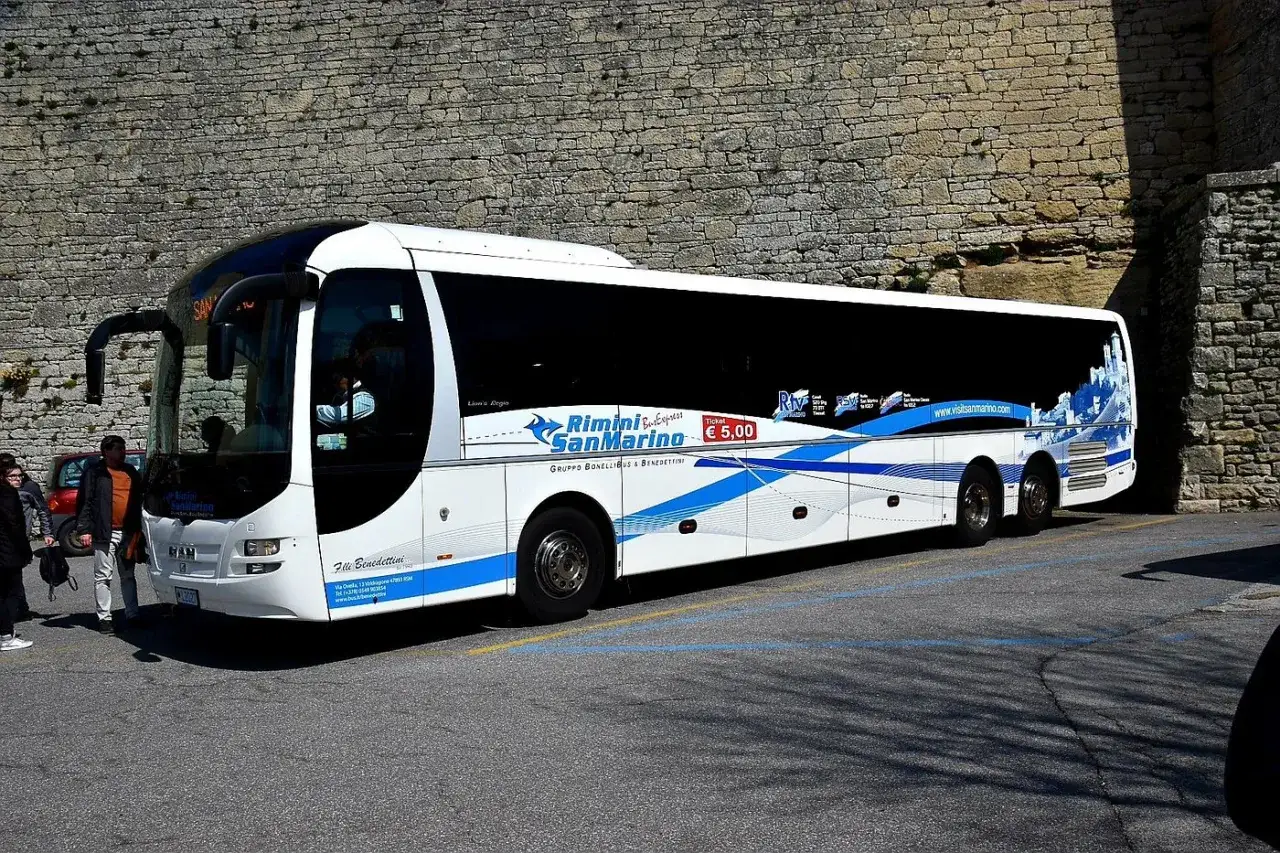 Autobus Rimini San Marino, con logo e prezzo del biglietto, parcheggiato vicino a un muro di pietra.