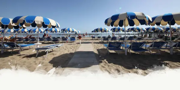 Ombrelloni a righe blu e bianche e lettini preparati per i visitatori al Delfini Beach Village Cattolica, con il mare sullo sfondo.