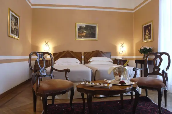 Camera elegante con due letti singoli, un tavolino con champagne e pasticcini, e sedie d'epoca. Un assaggio di lusso al Grand Hotel Rimini.