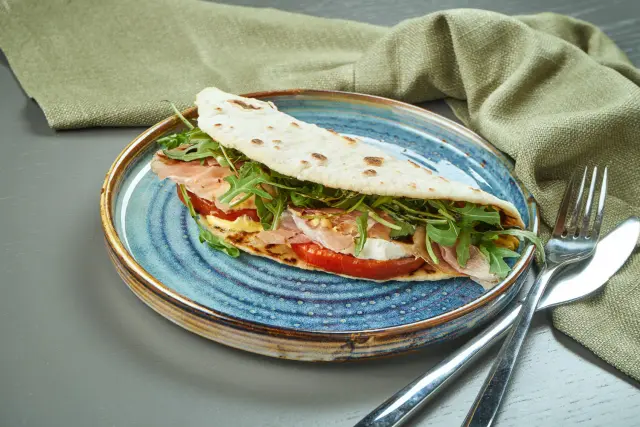 Piadina romagnola con prosciutto crudo, mozzarella, pomodoro e rucola. Un'ottima idea per cosa mangiare a Rimini, gustosa e fresca.