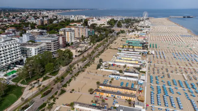 Vista aerea di una vasta spiaggia libera a Rimini, con file ordinate di ombrelloni e cabine colorate che si estendono fino al mare.
