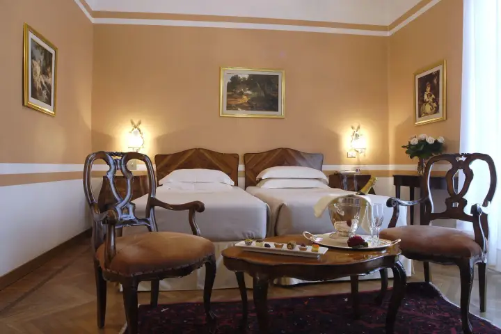 Camera elegante con due letti singoli, un tavolino con champagne e pasticcini, e sedie d'epoca. Un assaggio di lusso al Grand Hotel Rimini.
