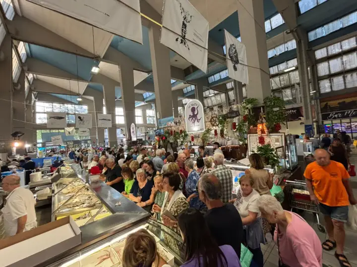 Folla vivace al mercato coperto di Rimini, con banchi di pesce fresco e gente che fa la spesa.