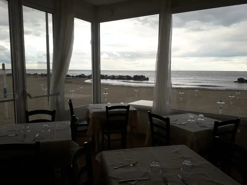 Tavoli apparecchiati in un ristorante con vista sulla spiaggia di Misano durante la bassa marea.