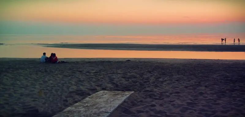 Alba a Rimini: una coppia seduta sulla sabbia guarda il mare calmo e il cielo colorato.