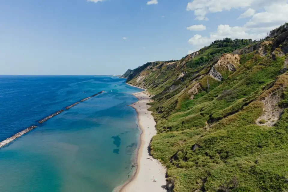 Costa verdeggiante del Monte San Bartolo bagnata da un mare azzurro. Spiaggia dorata e scogliere a picco.