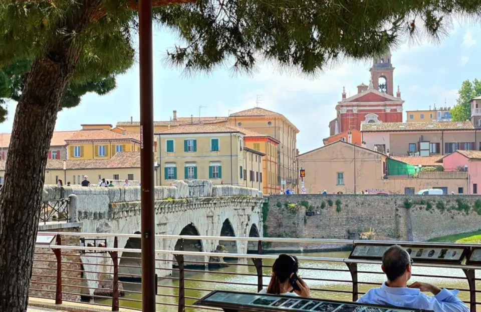 Ponte di Tiberio a Rimini, un luogo iconico per il Rimini Meeting, con persone che passeggiano e ammirano il panorama.